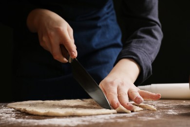 Photo of Woman cutting dough at wooden table, closeup. Cooking grissini