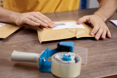 Post office worker sticking barcode on parcel at counter indoors, closeup