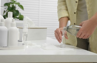 Photo of Woman pouring cosmetic product into plastic bottle at white countertop in bathroom, closeup. Bath accessories