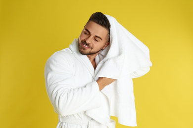 Photo of Young man in bathrobe drying hair with towel on yellow background
