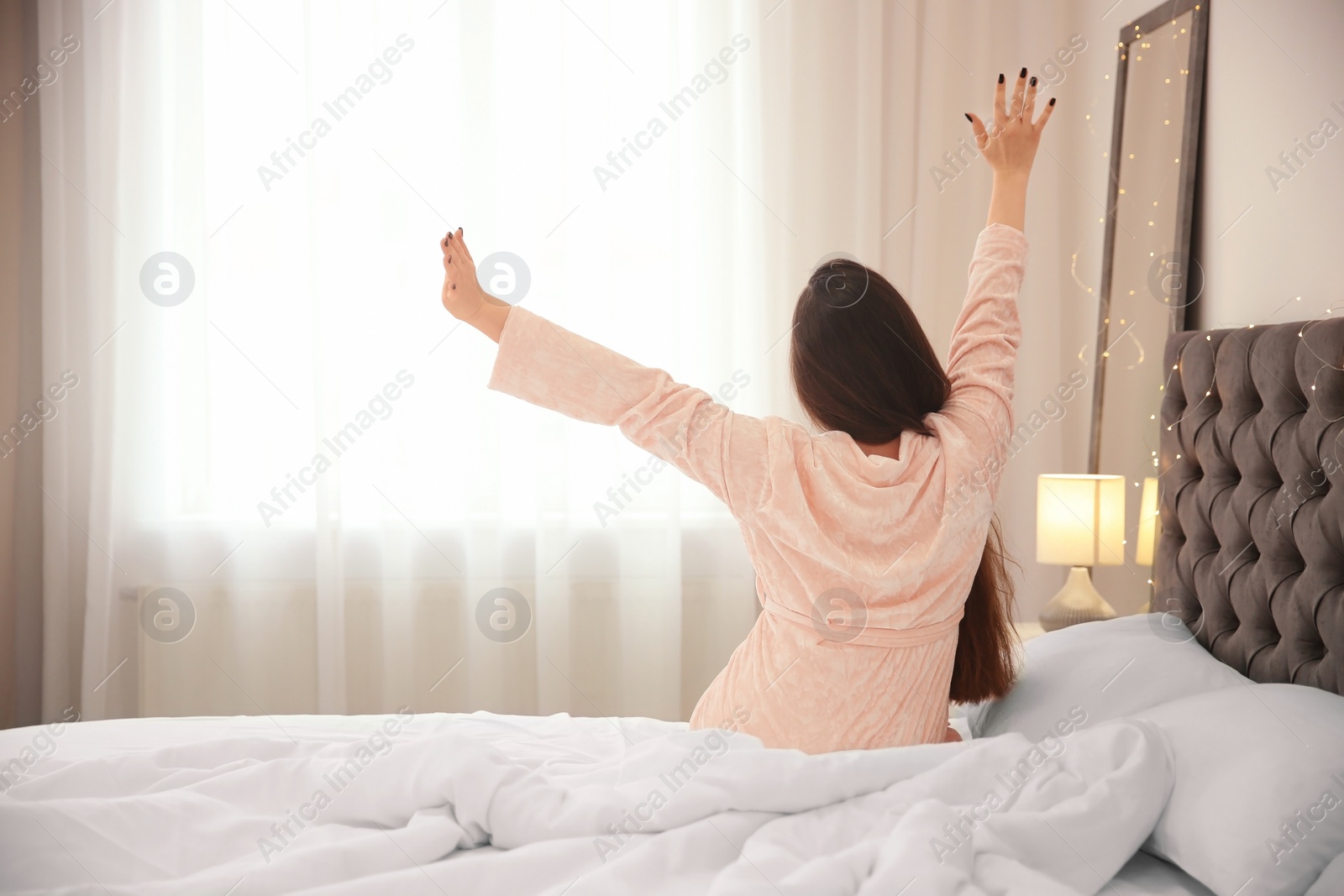 Photo of Young woman stretching on bed in hotel room