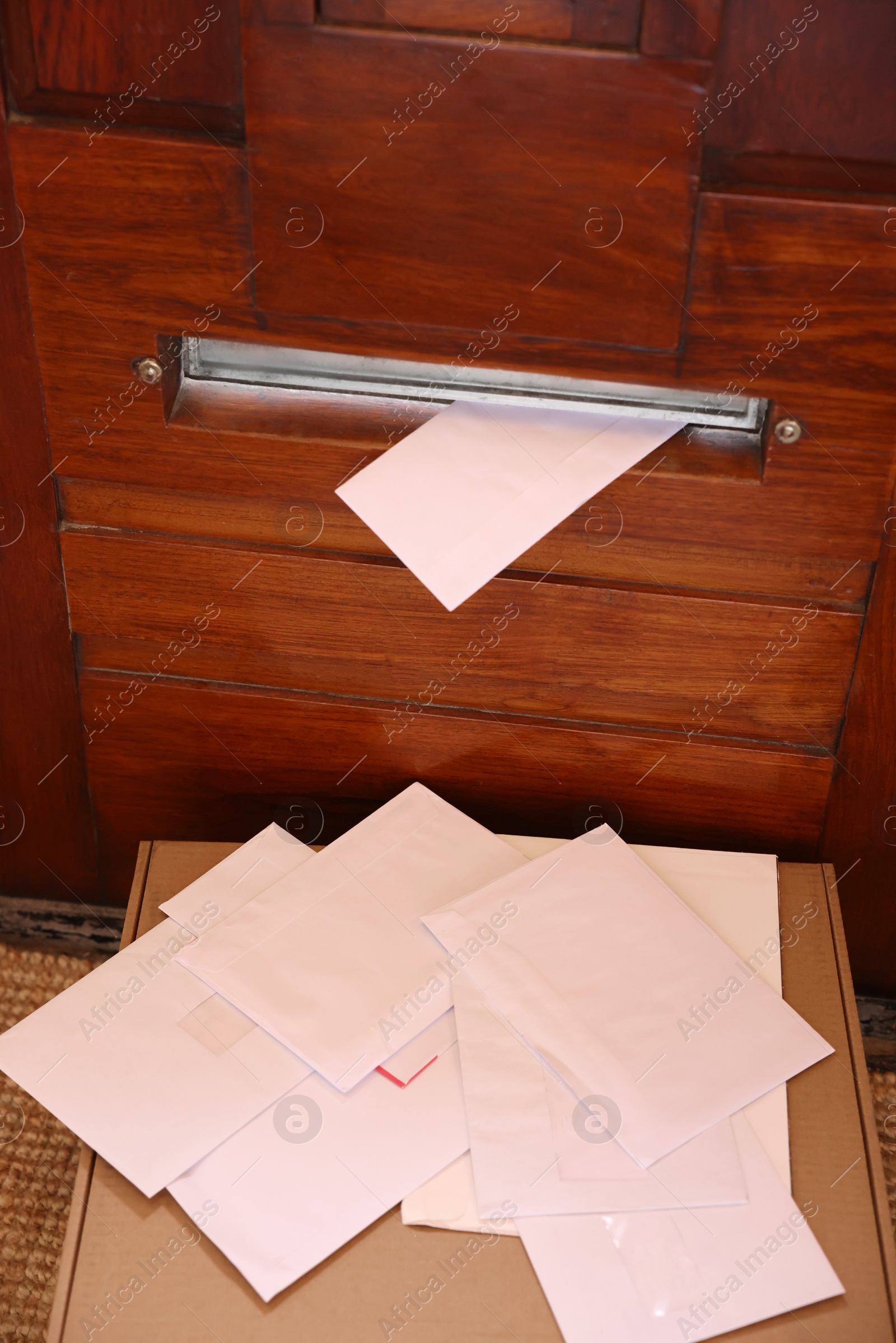 Photo of Wooden door with mail slot, many envelopes and cardboard indoors, above view