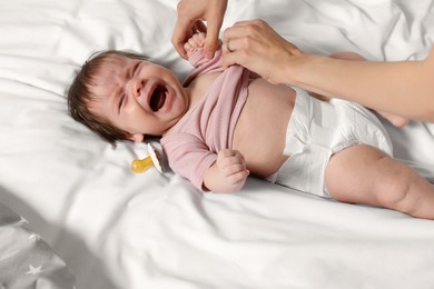 Photo of Mother putting clothes on crying daughter on bed, closeup