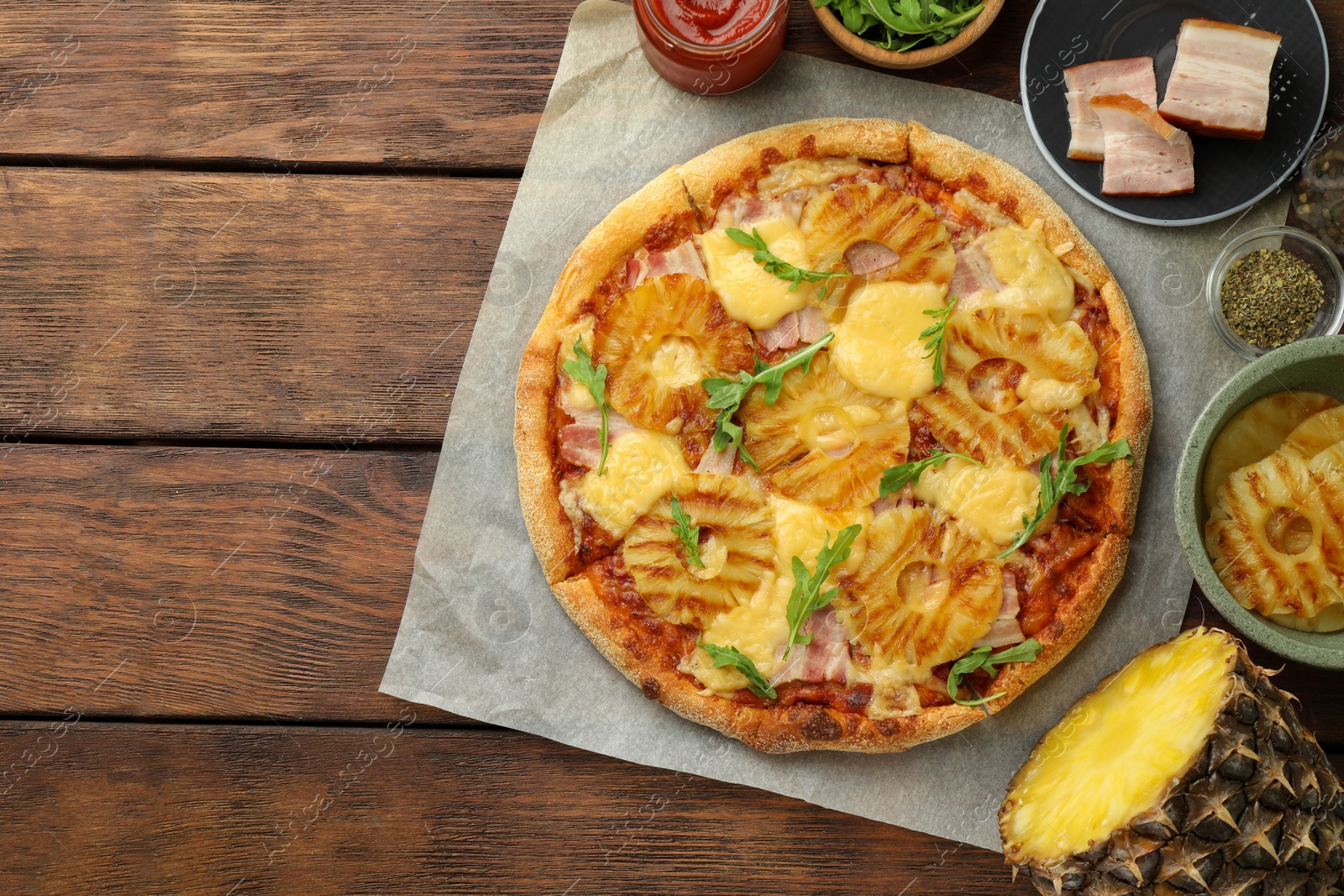 Photo of Delicious pineapple pizza and ingredients on wooden table, flat lay. Space for text