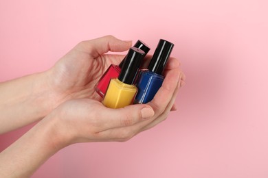 Photo of Woman holding nail polishes on pink background, closeup
