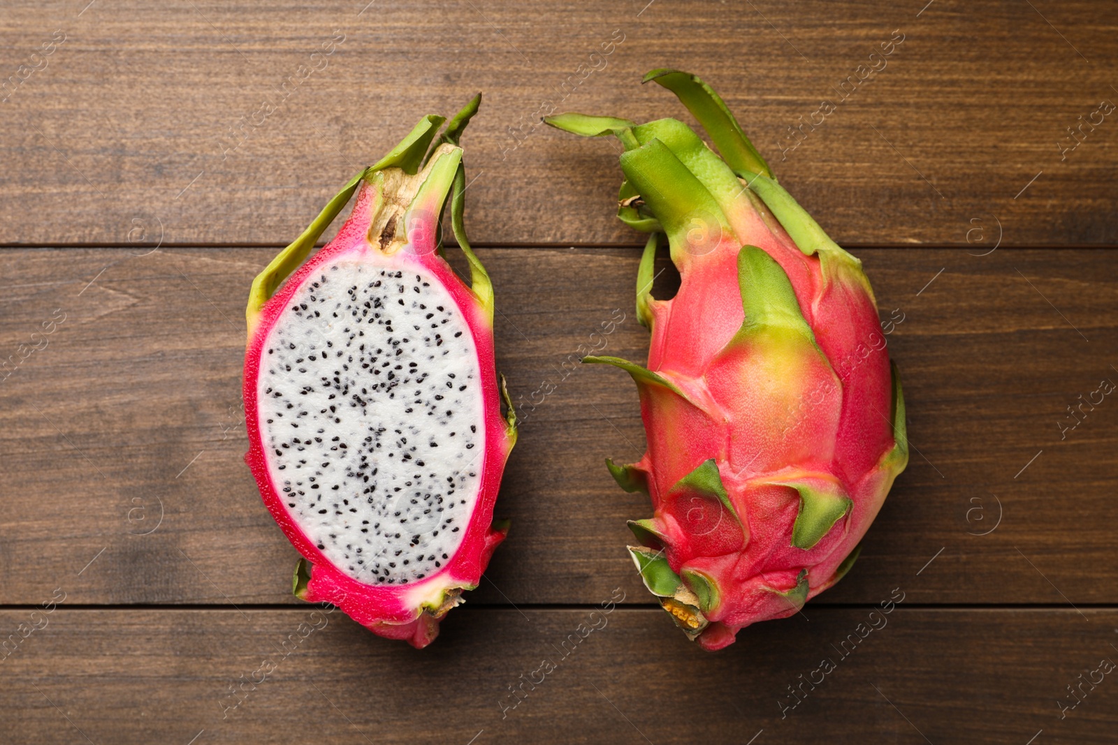 Photo of Delicious cut and whole dragon fruits (pitahaya) on wooden table, flat lay