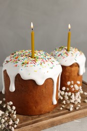 Tasty Easter cakes with burning candles on grey table