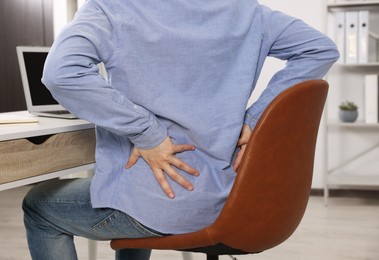 Man suffering from back pain while working with laptop in office, closeup. Symptom of scoliosis
