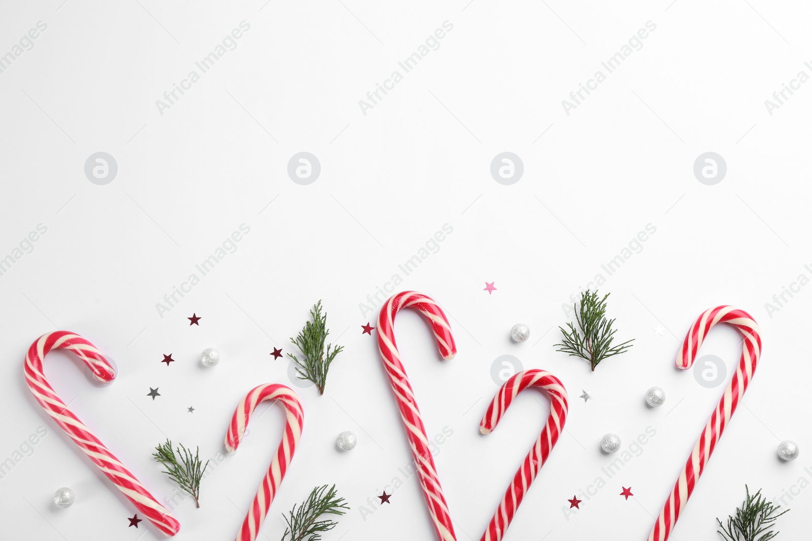 Photo of Candy canes and fir branches on white background, flat lay with space for text. Christmas treat