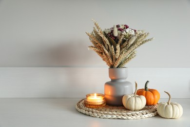 Photo of Beautiful bouquet of dry flowers, small pumpkins and candle on white table near light wall, space for text