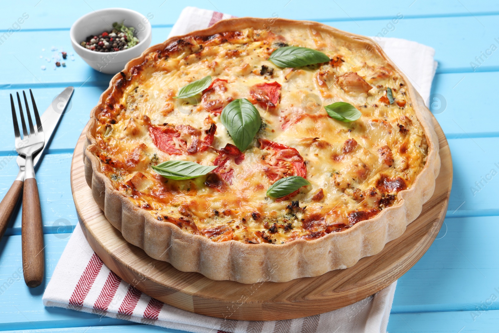 Photo of Tasty quiche with tomatoes, basil and cheese served on light blue wooden table, closeup