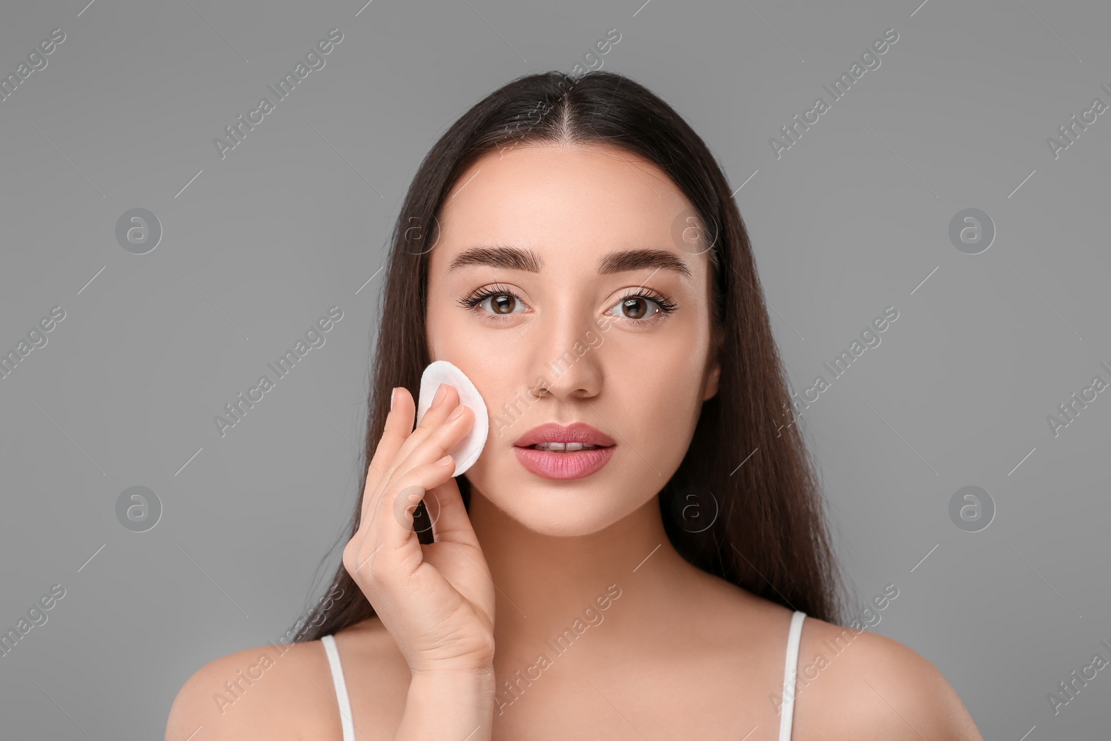 Photo of Beautiful woman removing makeup with cotton pad on gray background