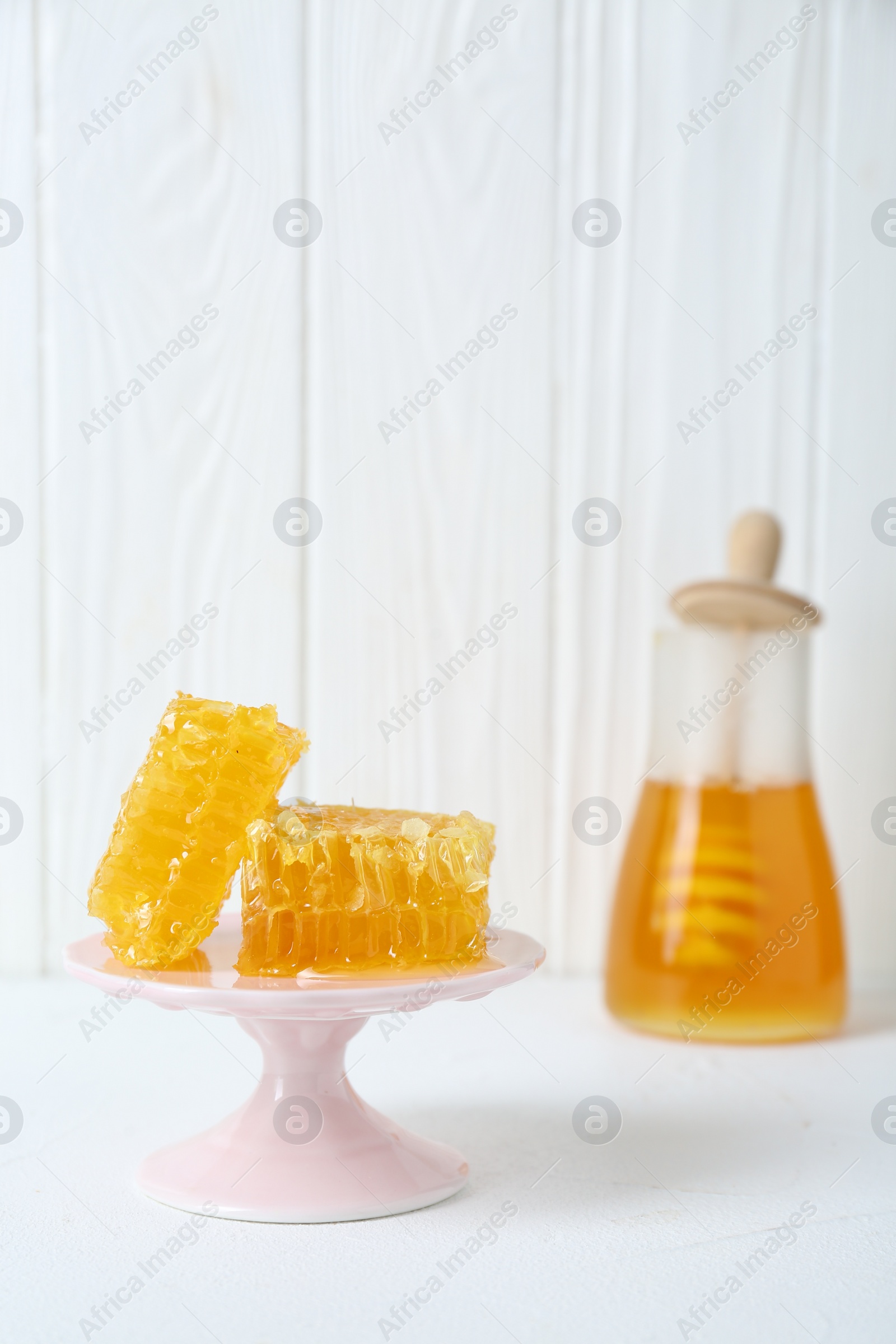 Photo of Stand with natural honeycombs and honey on white table, selective focus. Space for text