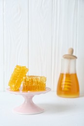 Stand with natural honeycombs and honey on white table, selective focus. Space for text
