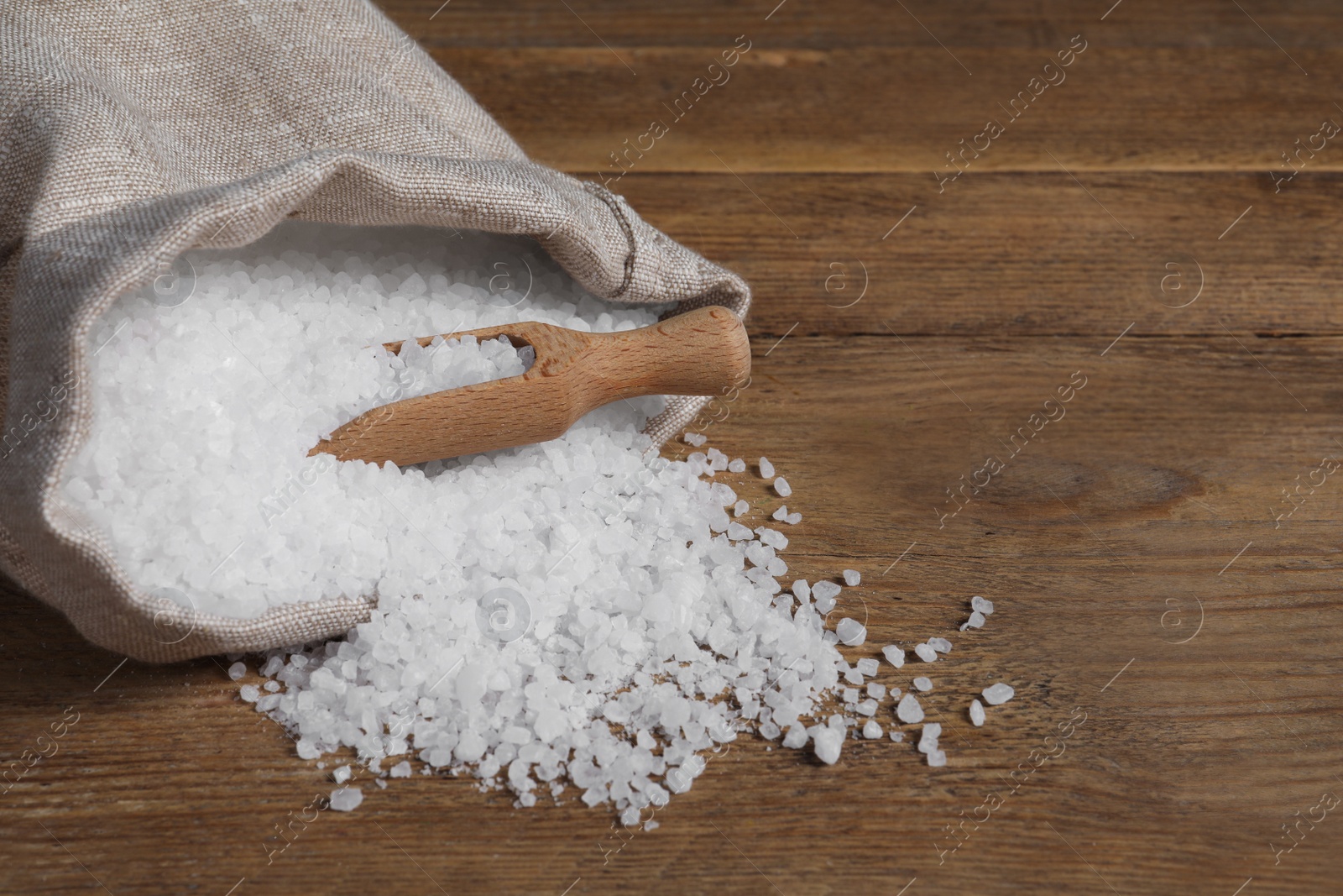 Photo of Bag of natural sea salt and scoop on wooden table. Space for text