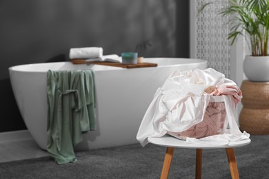 Photo of Laundry basket filled with clothes on table in bathroom. Space for text