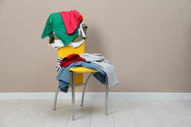 Photo of Different clothes on yellow chair near light grey wall, space for text