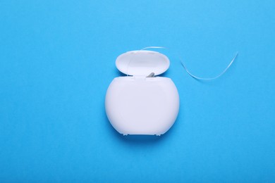 Container with dental floss on light blue background, top view