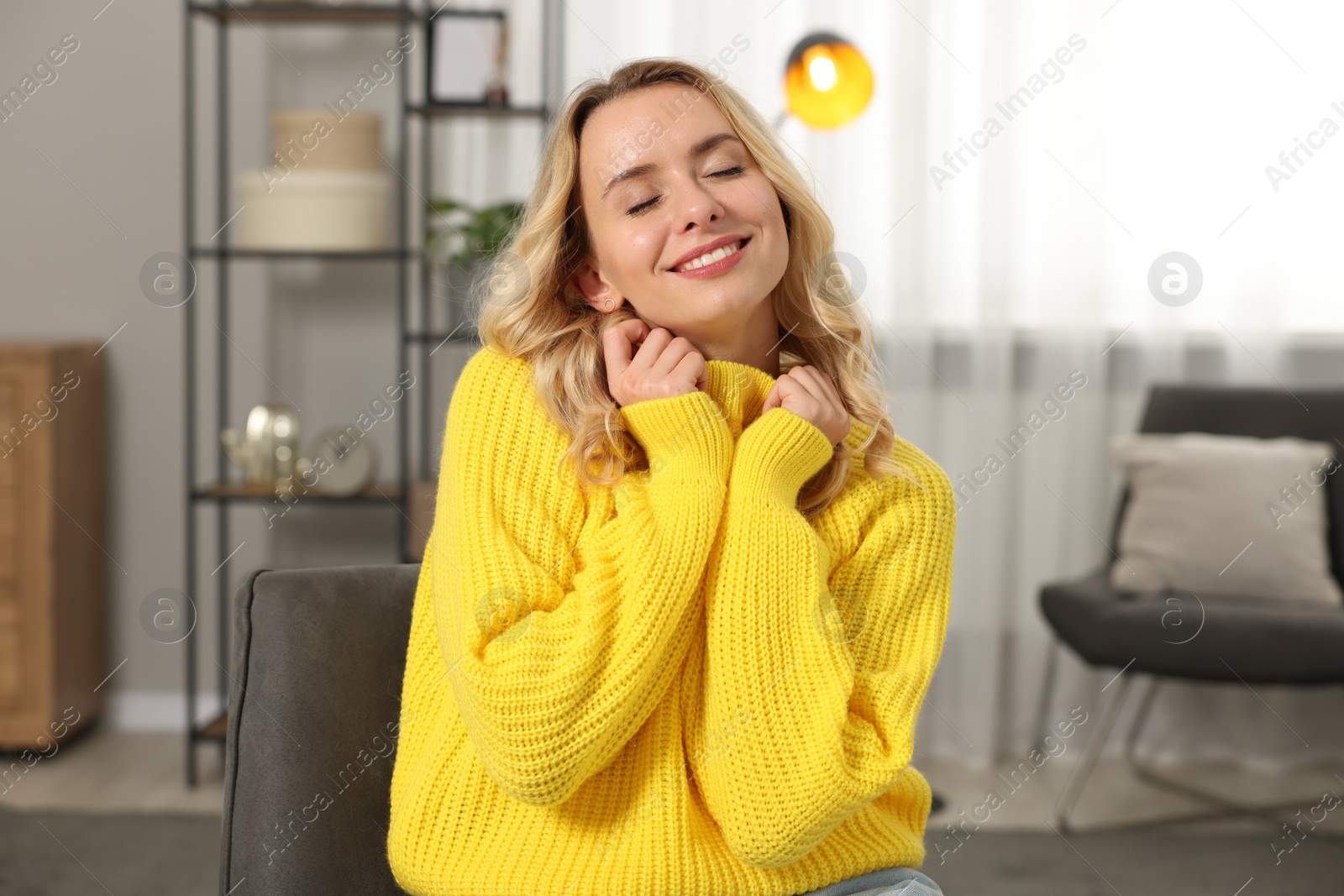 Photo of Happy woman wearing stylish warm sweater in armchair at home