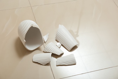 Photo of Broken white ceramic vase on floor indoors