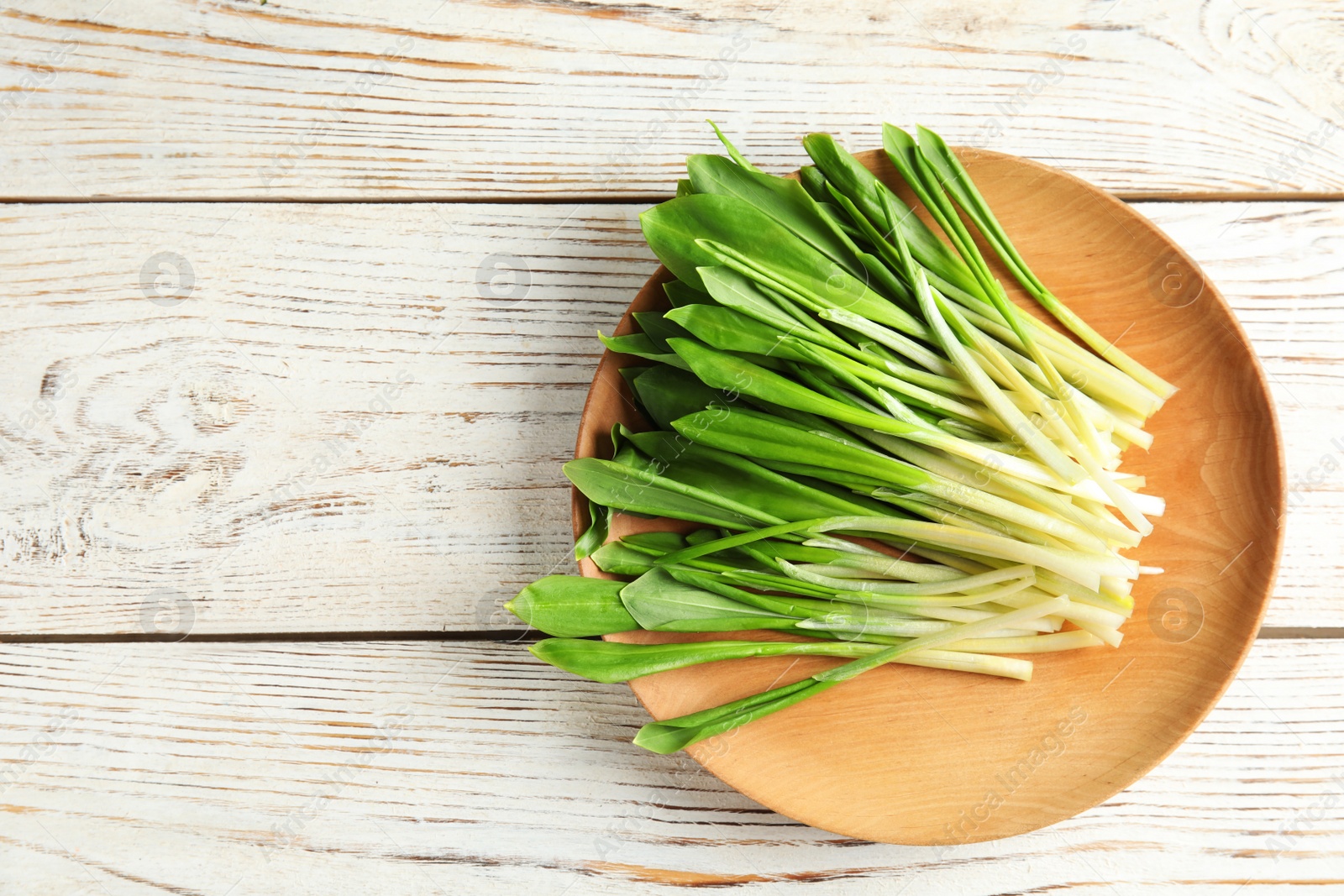 Photo of Plate with wild garlic or ramson on wooden table, top view. Space for text