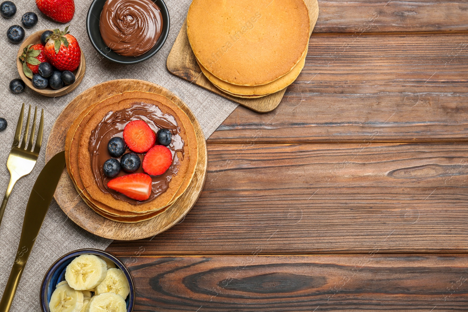 Photo of Tasty pancakes with chocolate paste, berries and banana on wooden table, flat lay. Space for text