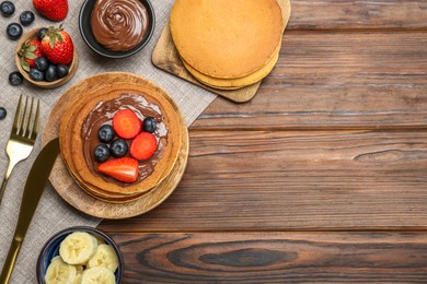 Photo of Tasty pancakes with chocolate paste, berries and banana on wooden table, flat lay. Space for text