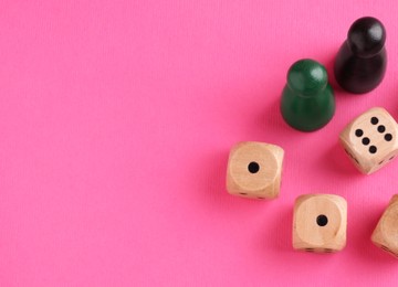 Wooden dices and color game pieces on pink background, flat lay. Space for text