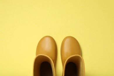 Photo of Yellow rubber boots on color background, flat lay. Space for text