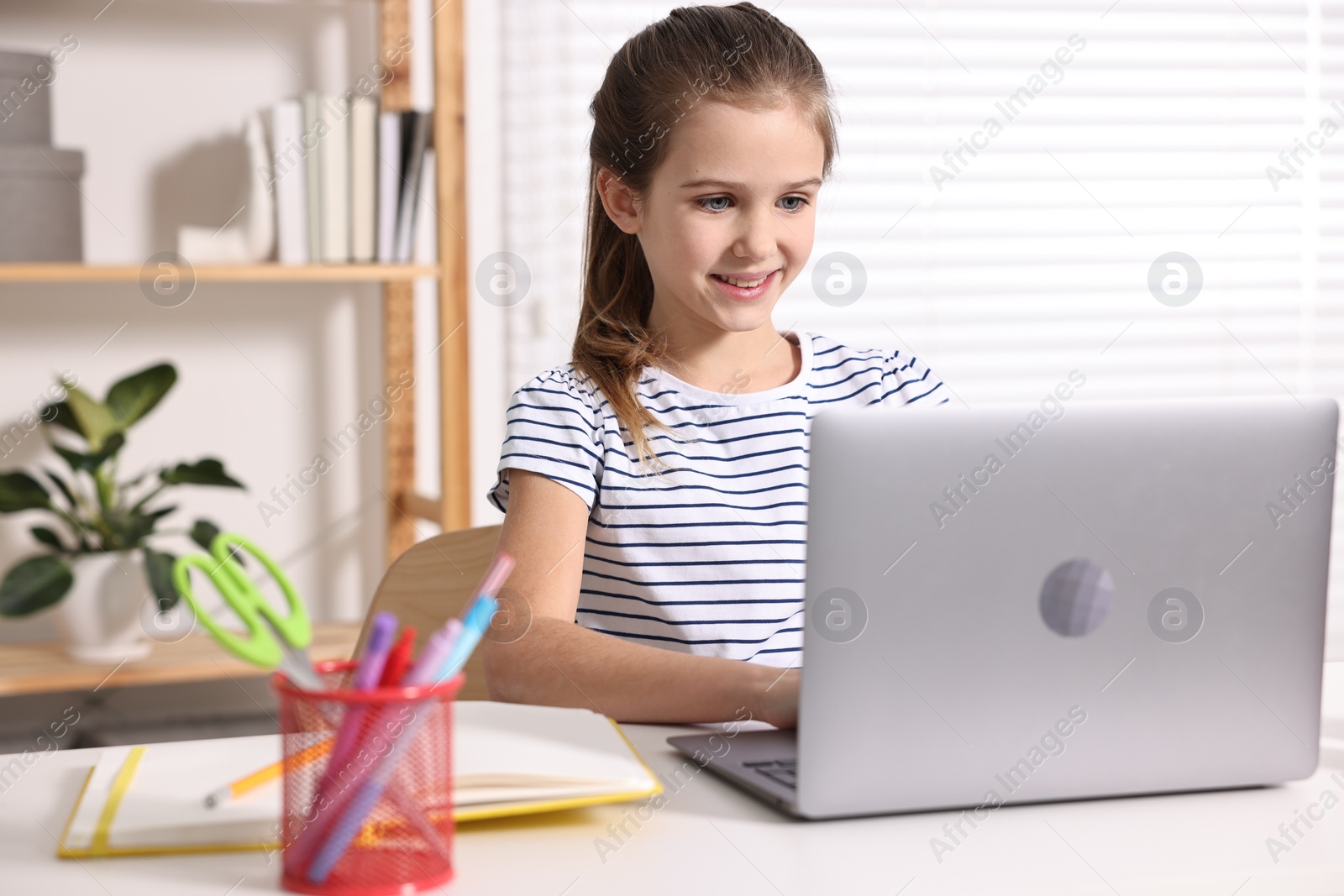 Photo of E-learning. Cute girl using laptop during online lesson at table indoors