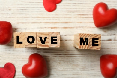 Photo of Cubes with phrase Love Me and red hearts on white table, flat lay