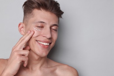 Photo of Handsome man with moisturizing cream on his face against light grey background. Space for text