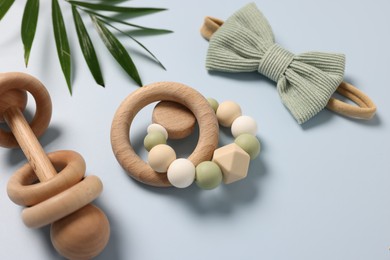 Photo of Baby accessories. Wooden rattles, scrunchy and palm leaf on light blue background, closeup