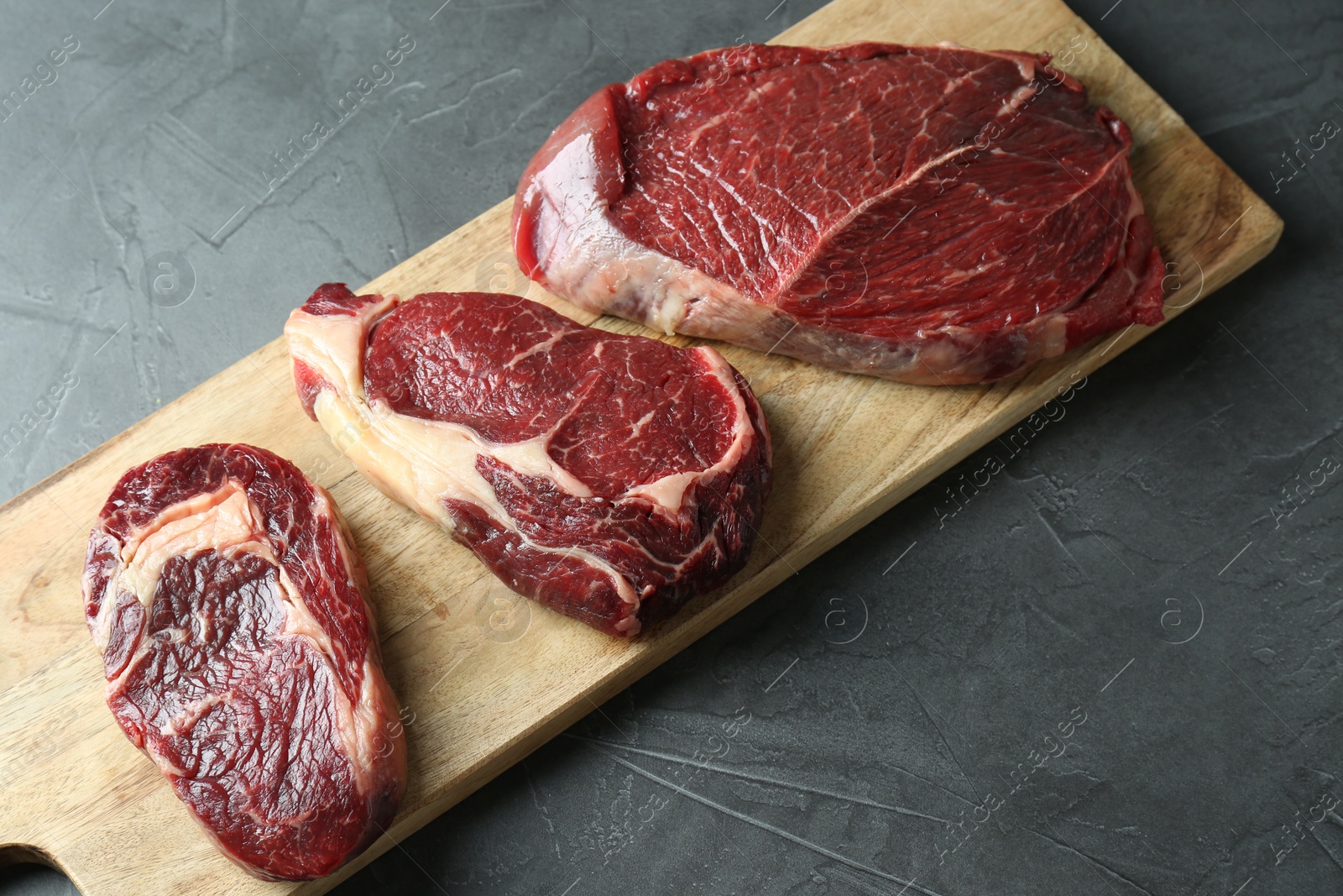 Photo of Wooden board with pieces of raw beef meat on grey table