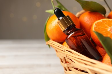 Bottle of tangerine essential oil and fresh fruits in basket, closeup. Space for text