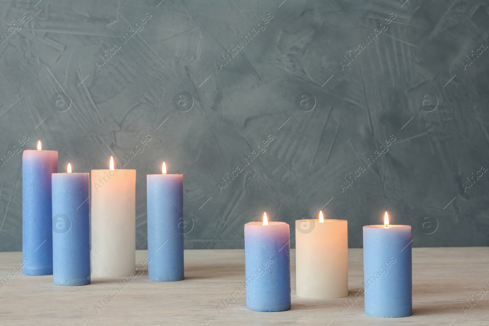 Photo of Burning candles on table against color wall with space for text