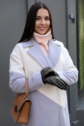 Photo of Portrait of beautiful young woman with leather gloves and stylish bag outdoors