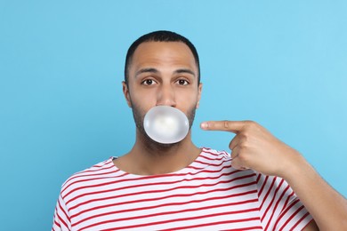 Portrait of young man blowing bubble gum on light blue background