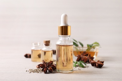 Photo of Bottles of essential oil, anise and seeds on white wooden table