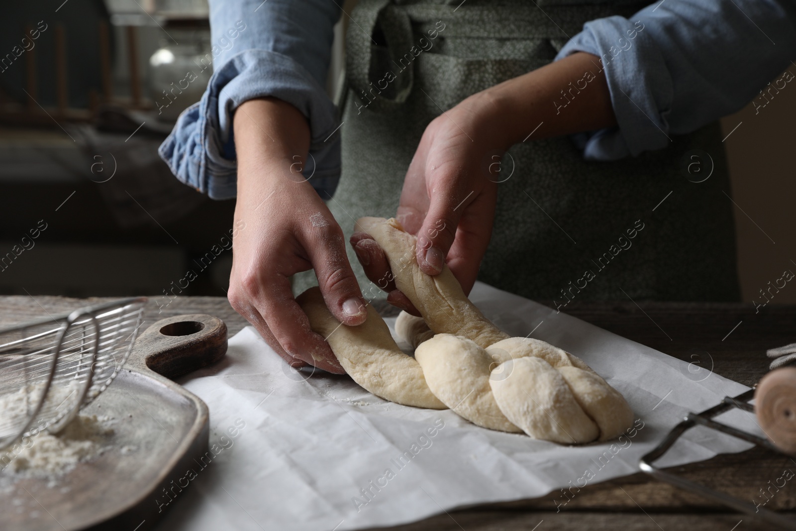 Photo of Woman making braided bread at wooden table indoors, closeup. Traditional Shabbat challah