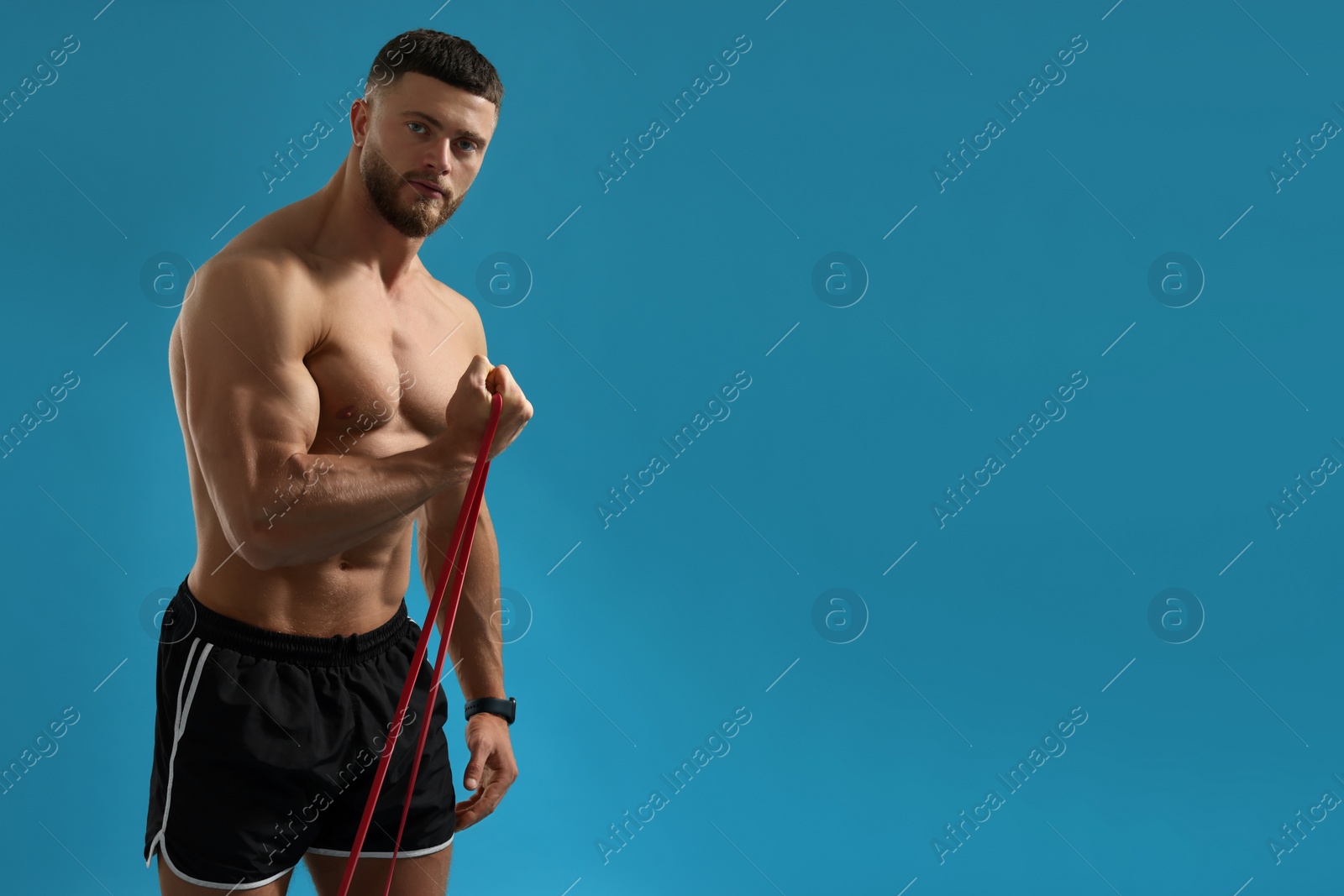 Photo of Muscular man exercising with elastic resistance band on light blue background. Space for text