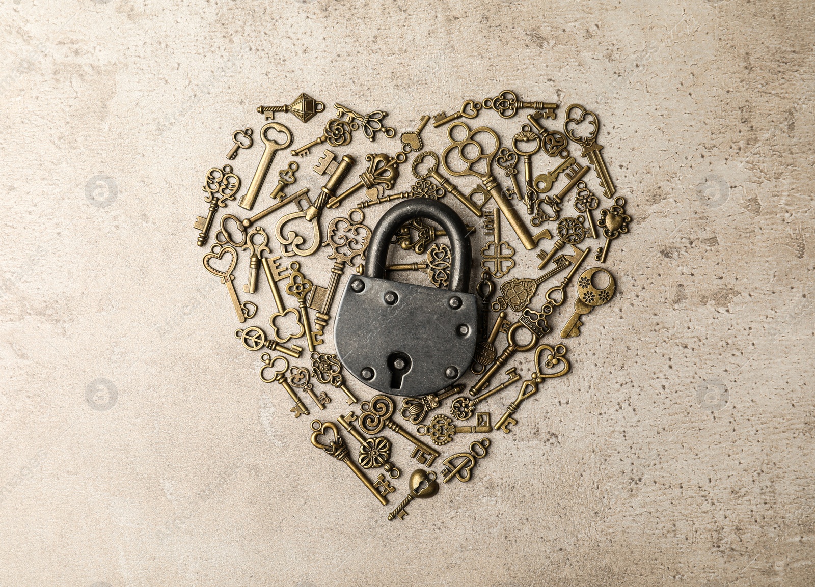 Photo of Heart made of keys and steel padlock on light stone background, top view. Safety concept