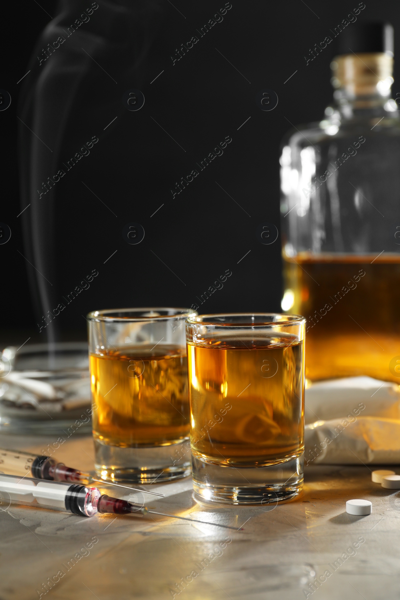 Photo of Alcohol and drug addiction. Whiskey in glasses, syringes, pills and cocaine on grey table