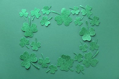 Photo of St. Patrick's day. Frame of shiny decorative clover leaves on green background, flat lay. Space for text