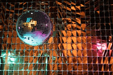 Photo of Shiny disco ball against foil party curtain under turquoise and orange light, space for text