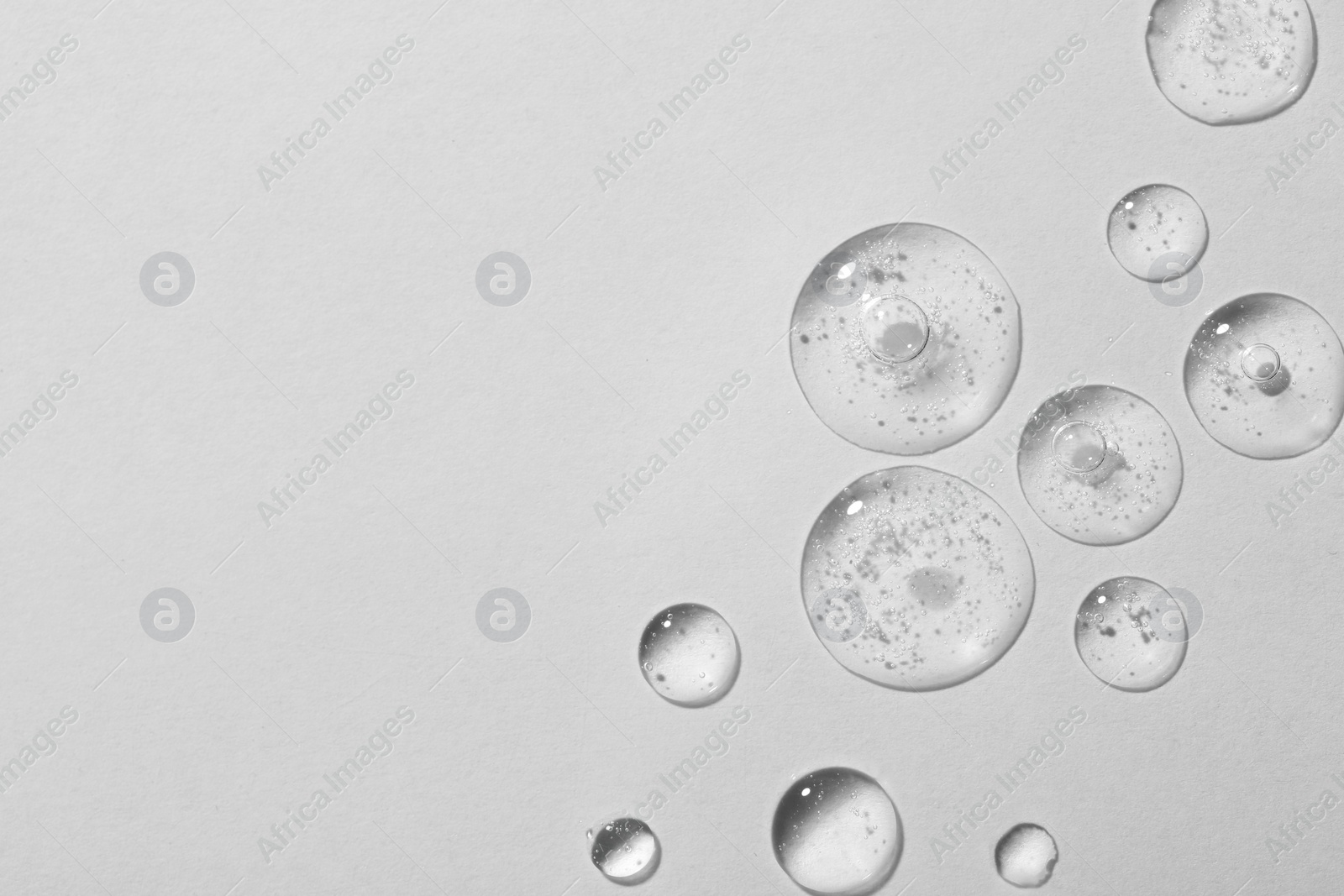 Photo of Drops of cosmetic serum on white background, top view. Space for text