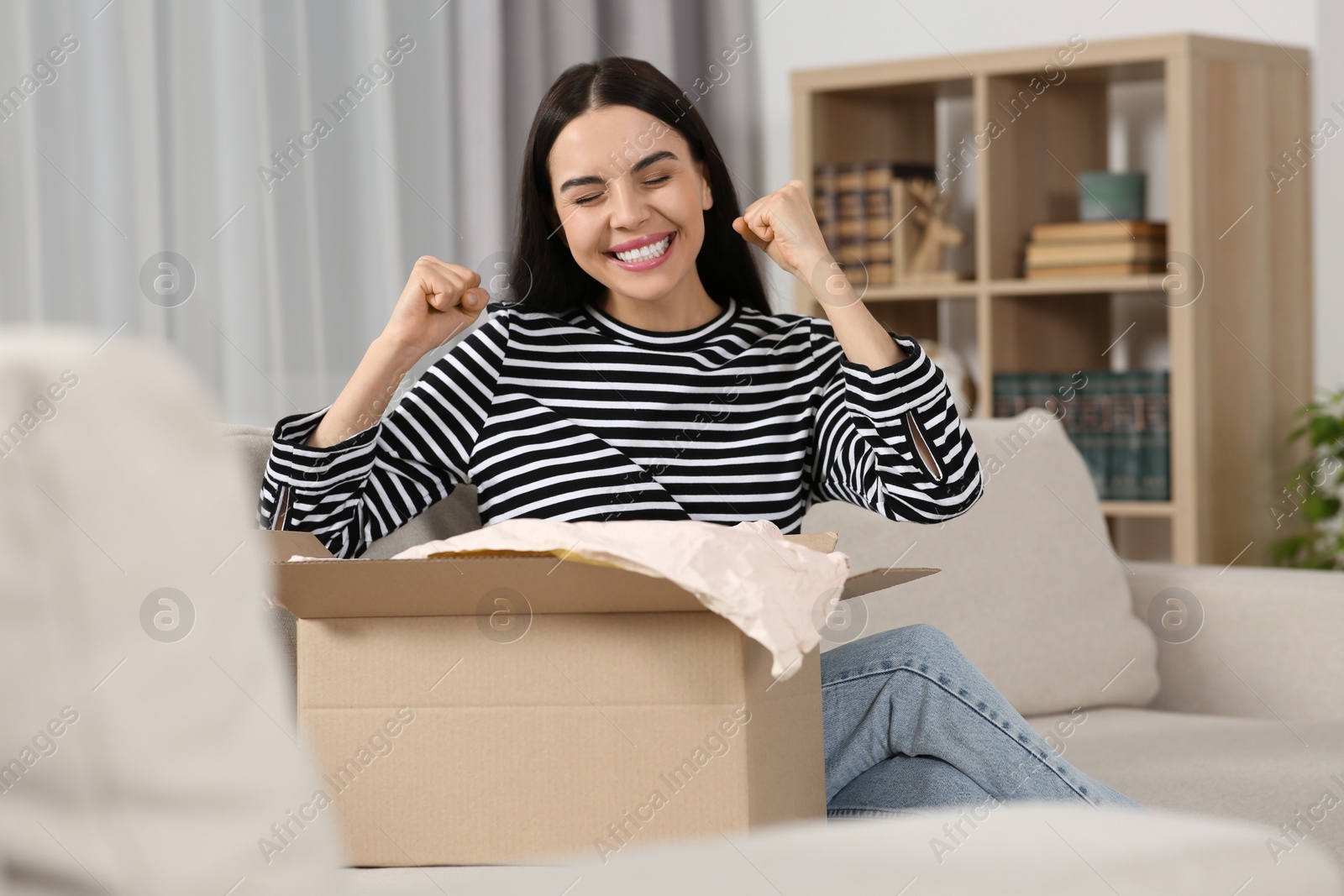 Photo of Emotional young woman with parcel at home. Internet shopping