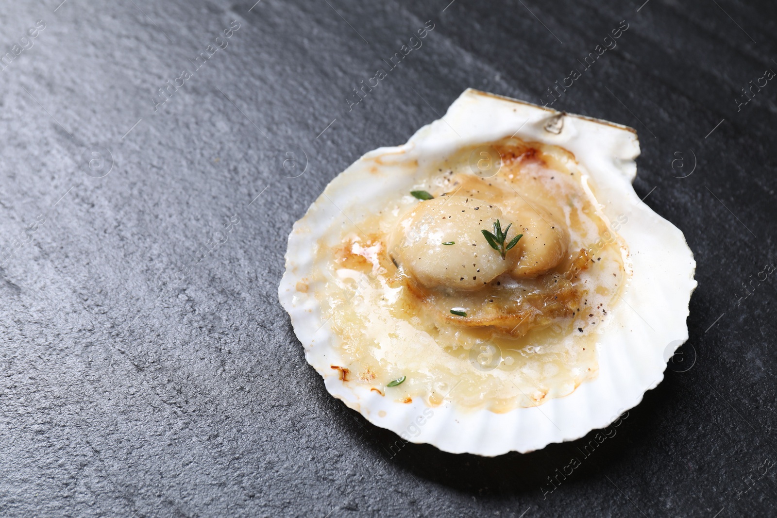 Photo of Fried scallop in shell on black table, closeup. Space for text