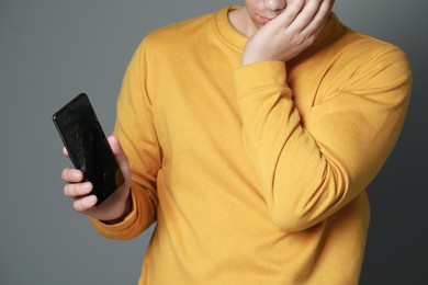 Photo of Man holding damaged smartphone on light grey background, closeup. Device repairing
