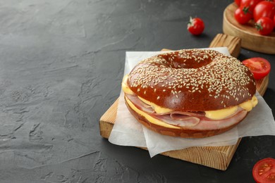 Photo of Delicious bagel with ham and cheese on grey textured table, space for text